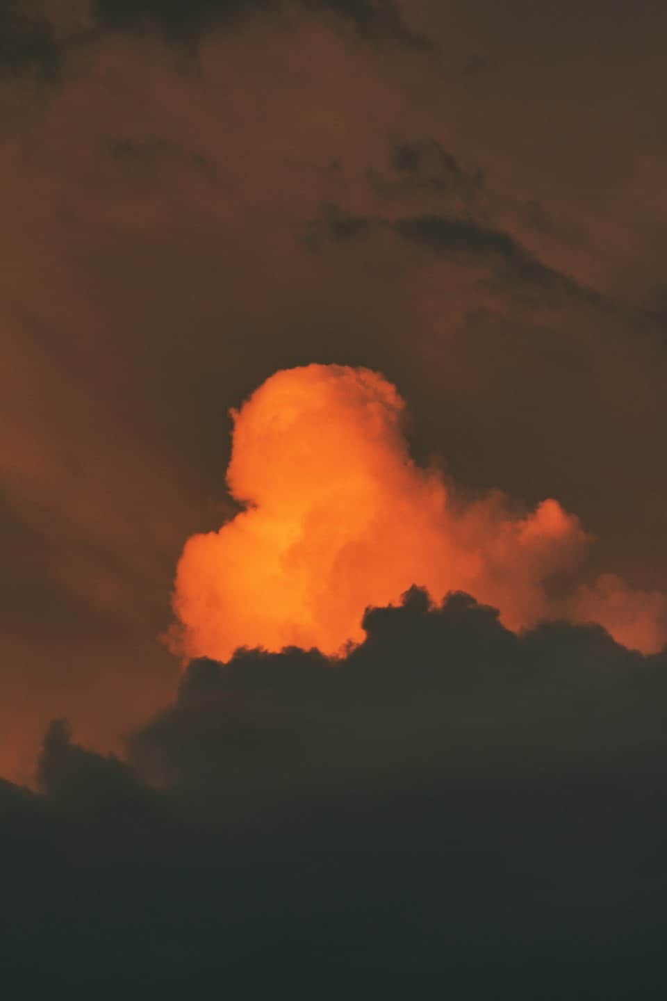 Eine leuchtend orangefarbene Wolke strahlt vor einem dunklen Himmel.